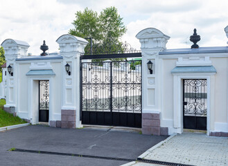 Elegant black metal gates at the entrance to a luxurious estate with stone columns and a landscaped driveway