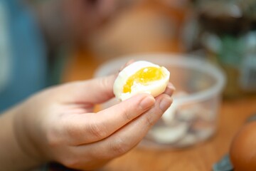 Woman holding a soft-boiled egg, bitten in half during a healthy breakfast