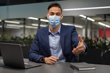 A middle eastern manager in a protective face mask is extending his hand towards the camera.