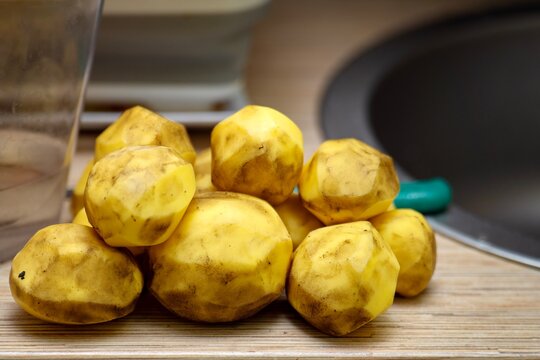 A pile of peeled, unwashed potatoes with soil traces, ready for cleaning in the sink
