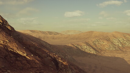 A breathtaking expanse of arid land unfolds, featuring rugged mountains and deep valleys under a golden sky. Shadows dance across the rocky ground, highlighting natures beauty at dusk.