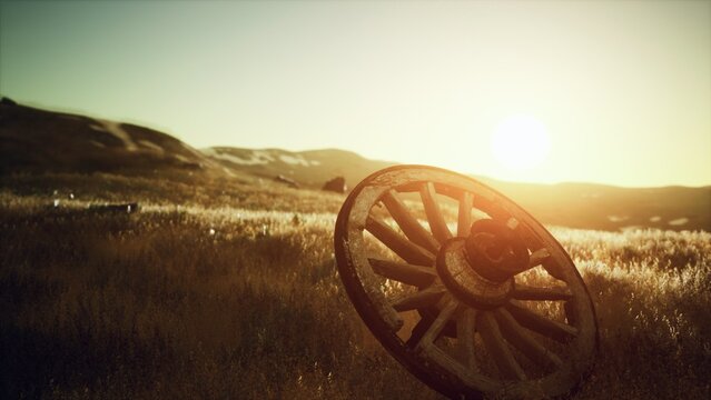 A weathered wagon wheel rests in a golden field as the sun sets on the horizon. The warm light casts a magical glow over the tranquil landscape, evoking a sense of nostalgia and peace.