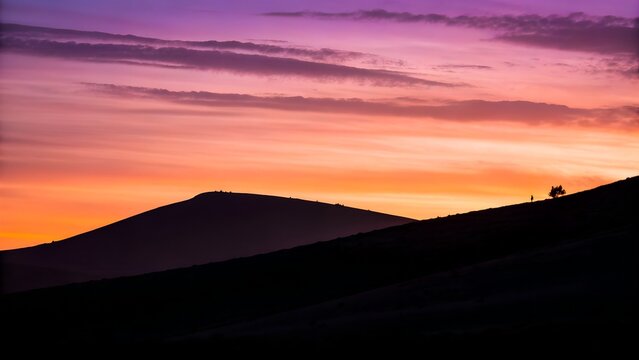 Silhouetted hikers ascend a mountain ridge against a vibrant purple and orange sunset sky