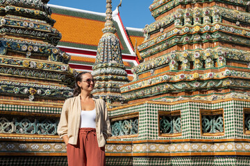 Smiling woman standing near ornate temple towers decorated with ceramics, wearing summer clothes, cultural travel and self discovery concept