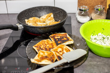 Savory lavash pastries with cottage cheese are cooked in a frying pan and cooled on a plate, with a bowl of cheese and herb filling nearby