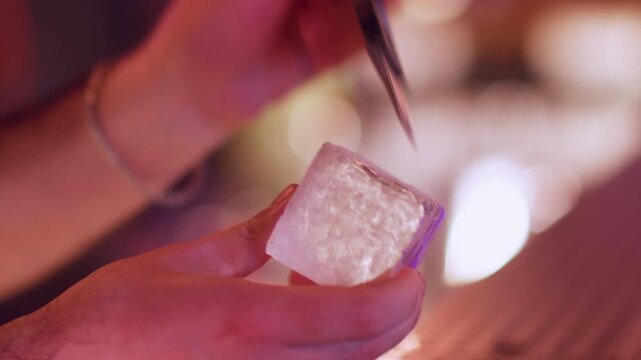 Cooling alcohol. Preparing cold drink. Bartender hand using chipper making textured huge cube for refreshing cocktail. Professional bar picks chisel.