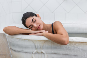 Woman relaxing in a marble bathtub at a hot springs spa with serene expression