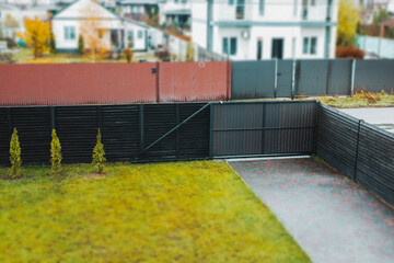 Modern home exterior with a black fence and gate, green lawn in a residential neighborhood. A...
