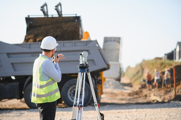 Engineer surveying construction site with dump truck operating