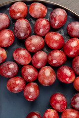 torn red grapes in drops of water on a blue plate , wet ripe and delicious red grapes on a plate on a black slate board