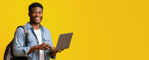 A young man stands with a laptop, smiling broadly. He wears a casual outfit and a backpack, radiating a positive vibe against a bright yellow background.