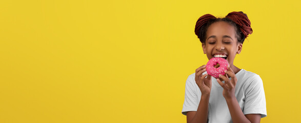 Girl with braided hair smiles widely while holding a pink donut. The cheerful yellow background enhances her happy expression. She clearly enjoys her tasty treat in this vibrant setting.