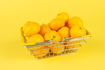 Fresh Kumquats Overflowing in Metal Basket on Vibrant Yellow Background