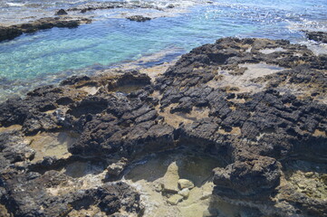 Rocky coastline with clear shallow waters and sunlight reflections, serene natural coastal landscape, copy space