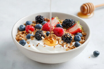 Bowl of yogurt topped with granola, blueberries, raspberries, blackberries, and flowing honey, captured in bright natural light for fresh breakfast visuals.