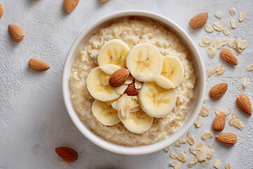 Creamy oatmeal topped with banana slices and almonds, surrounded by scattered oats and nuts, photographed in soft natural light for warm breakfast scenes.