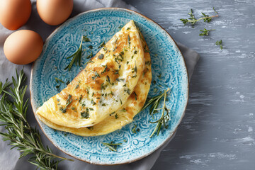 Folded omelette with cheese and herbs on a blue ceramic plate, surrounded by fresh eggs and sprigs, photographed in soft daylight for bright breakfast imagery.