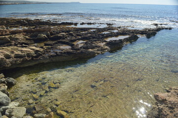 Crystal clear tidal pool on rocky shore with shimmering water under bright sunlight, serene coastal landscape, copy space