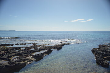 Scenic view of rocky tidal pools and calm sea under a bright blue sky, tranquil coastal landscape, copy space