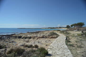 Picturesque coastal pathway leading to a rocky shore and clear blue sea under sunny sky, serene nature landscape, copy space