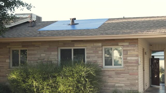 A house roof is leaking and a tarp is installed as a temporary cover.