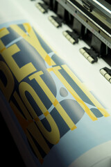 Large format vinyl printer printing yellow and black text on white material with sensor and rollers visible