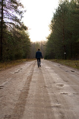 Man Walking Alone on a Dirt Road Through the Forest