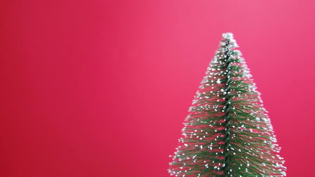 Rotating miniature Christmas tree on a static frame with clean red copy space, perfect for festive backgrounds and design layouts
