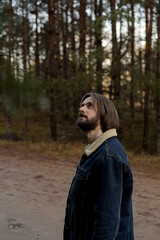 Man Looking Up in Pine Forest with Denim Jacket and Beard