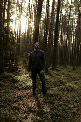 Man walking in a forest at sunset, with sunlight filtering through the trees