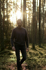 Man walking in a forest at sunset, with sunlight filtering through the trees