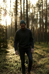 Man walking in a forest at sunset, with sunlight filtering through the trees