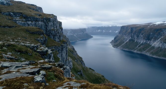 Dramatic landscape of a deep, calm fjord with rugged cliffs and overcast sky