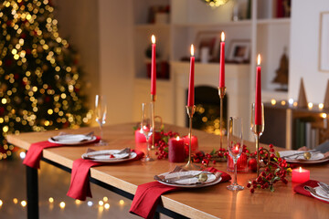Stylish Christmas table setting with plates, glasses and burning candles in festive decorated room. Bokeh effect