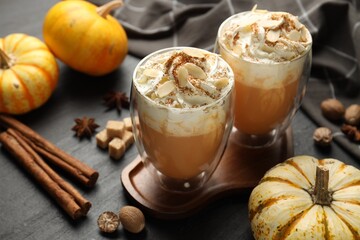 Tasty pumpkin latte with whipped cream, spices and fresh vegetables on black table, closeup