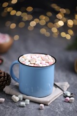Tasty cocoa with marshmallows on grey table against blurred Christmas lights, closeup