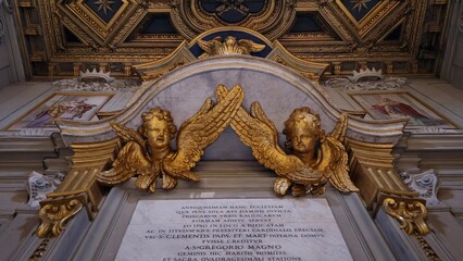 Rome, Italy - 11 January 2025. Gilded cherubs with spread wings sit above a Latin dedication plaque...