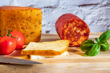 Sliced kulen and semi-hard cheese arranged neatly on a plate, garnished with fresh basil leaves. The vibrant colors of the red cured sausage, creamy-yellow cheese, and green basil create a visually ap