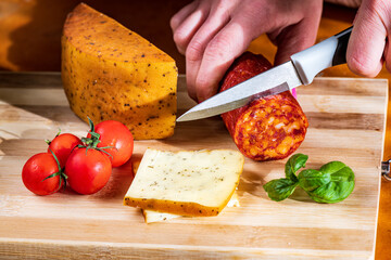 Sliced kulen and semi-hard cheese arranged neatly on a plate, garnished with fresh basil leaves. The vibrant colors of the red cured sausage, creamy-yellow cheese, and green basil create a visually ap