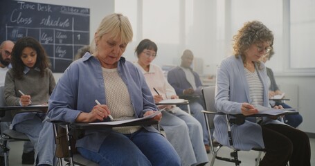 Obraz premium Mature Multicultural Students Attending Class, Taking Notes and Listening to Instructor. Concept Adult Training, Lifelong Learning, Professional Growth, Modern Educational Environment. Static Shot.