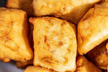 Golden, freshly fried fritters arranged on a plate, featuring a crispy exterior and a soft, airy inside. Warm lighting enhances their rich golden color and homemade rustic appearance.