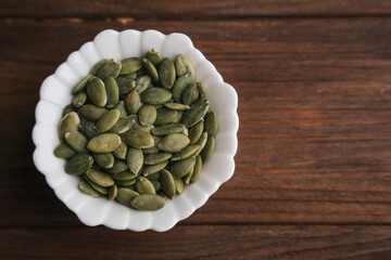 Pumpkin seeds in a white bowl on a wooden table ready for healthy snacking and cooking