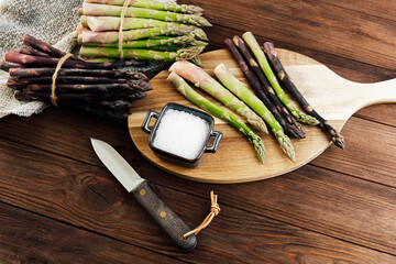 Fresh asparagus and sea salt on a wooden board with knife on rustic kitchen table
