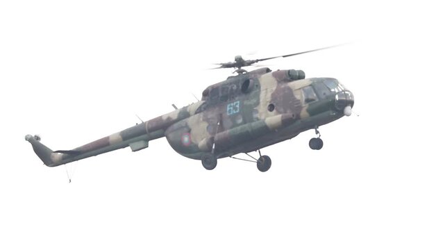 Shot of a Mil Mi-8 military transport helicopter with camouflage paint flying against a bright, white sky background.

