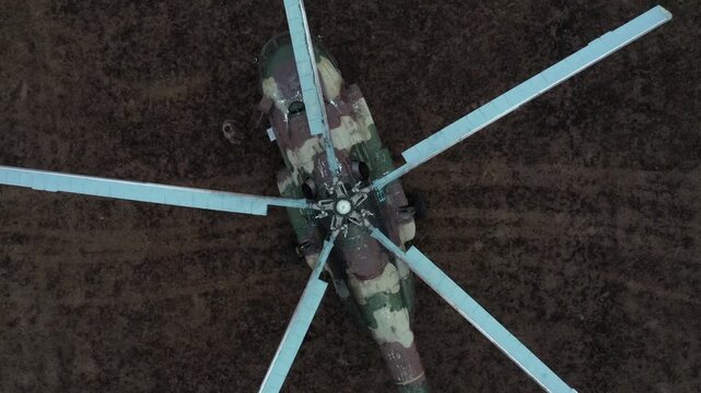 Aerial view of a military transport helicopter (Mi-8) landed in a vast, brown field during troop training operations, with mountains and solar panels visible.