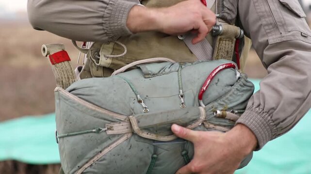 Close-up of a paratrooper securing and adjusting the harness and chute on their parachute rig before a jump, demonstrating careful preparation for airborne operations or skydiving.

