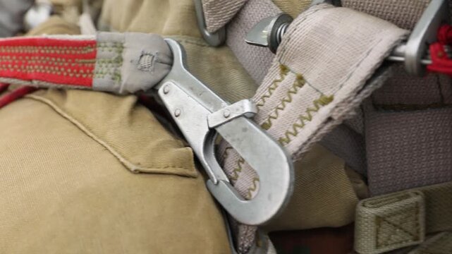 Close-up of a paratrooper securing and adjusting the harness and chute on their parachute rig before a jump, demonstrating careful preparation for airborne operations or skydiving.

