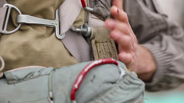 Close-up of a paratrooper securing and adjusting the harness and chute on their parachute rig before a jump, demonstrating careful preparation for airborne operations or skydiving.

