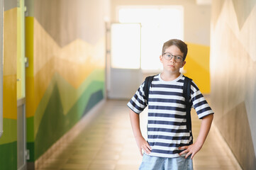 Confident student wearing glasses and backpack standing in school hallway