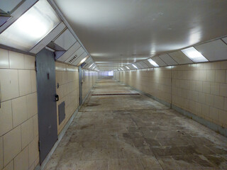 A long underground corridor with fluorescent lights, beige tiled walls and metal doors.